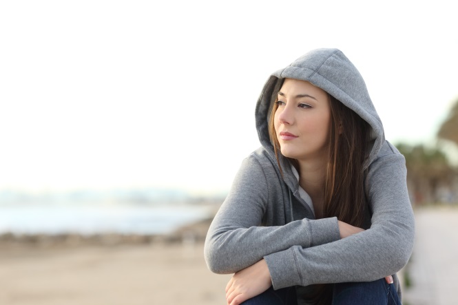 woman in a hoodie sitting on a beach